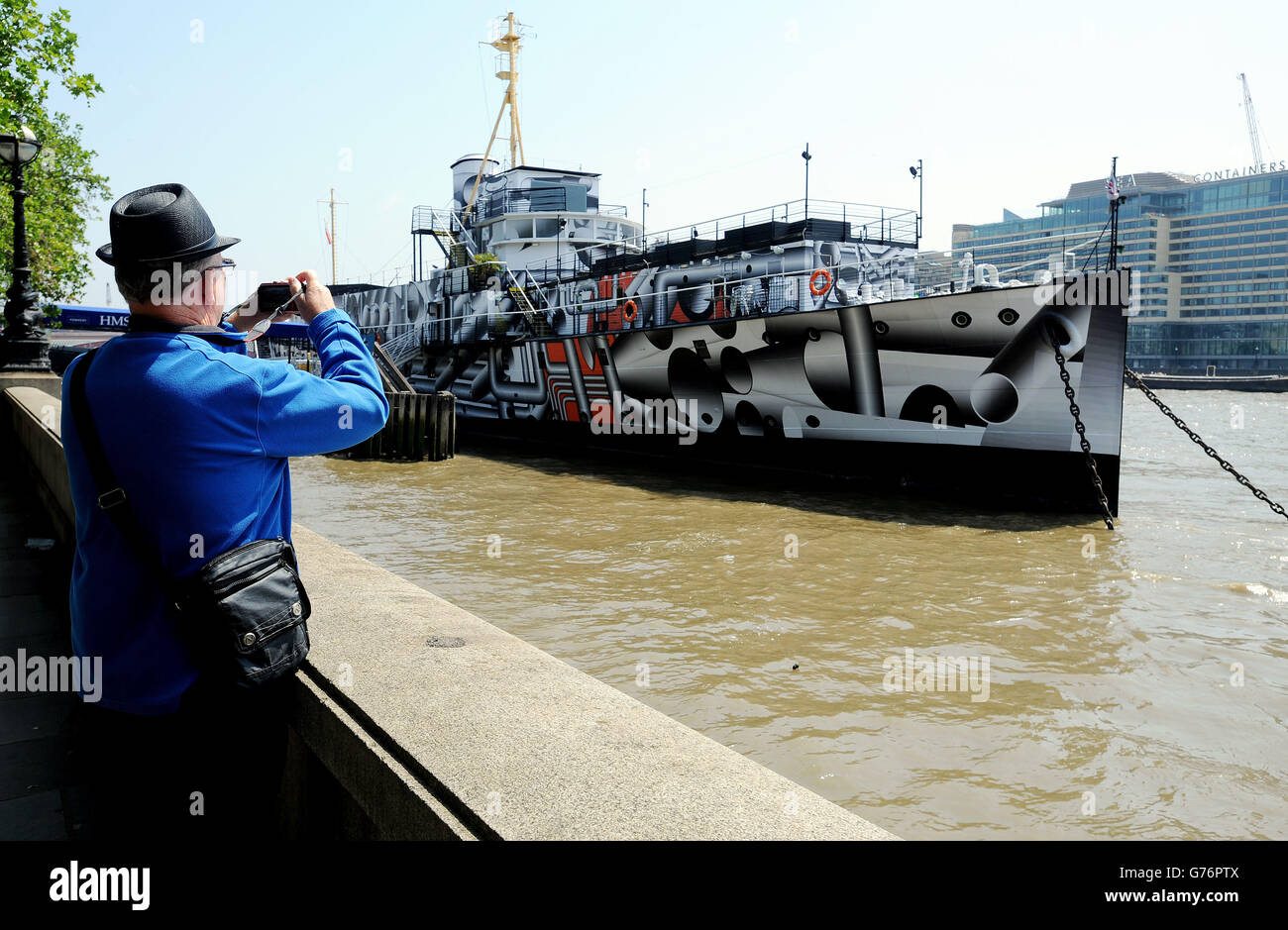 Un uomo si ferma a fotografare la nave da guerra della prima Guerra Mondiale, il presidente della HMS (1918), che è diventato un'opera d'arte pubblica sull'argine di Londra, chiamata Dazzle Ship London dall'artista Tobias Rehberger, la nave, una delle ultime tre navi da guerra della prima guerra mondiale, È stato coperto in stampa camouflage abbagliante come parte di 14 - 18 ora, un programma di eventi per celebrare il centenario della prima guerra mondiale Foto Stock