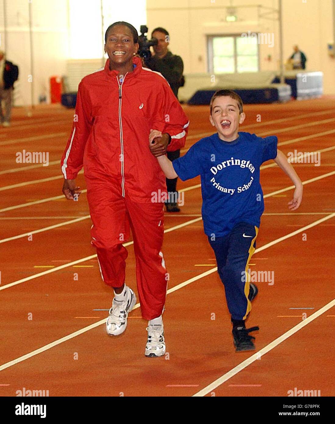 Philip Milman, 10 anni, ha un po' di aiuto professionale da parte del triplice jumper olimpico Ashia Hansen, mentre i bambini della Dorrington Primary School, Perry Barr, Birmingham, provano la pista, dopo che Mark Lewis-Francis ha rotto il record indoor di 100 metri in 10.34 secondi. * il tentativo da record faceva parte della cerimonia ufficiale di apertura del nuovo stabilimento da 3.3 milioni di persone all'Alexandra Stadium di Birmingham, offrendo agli atleti l'opportunità di allenarsi per sprint, saltare e tirare. Foto Stock
