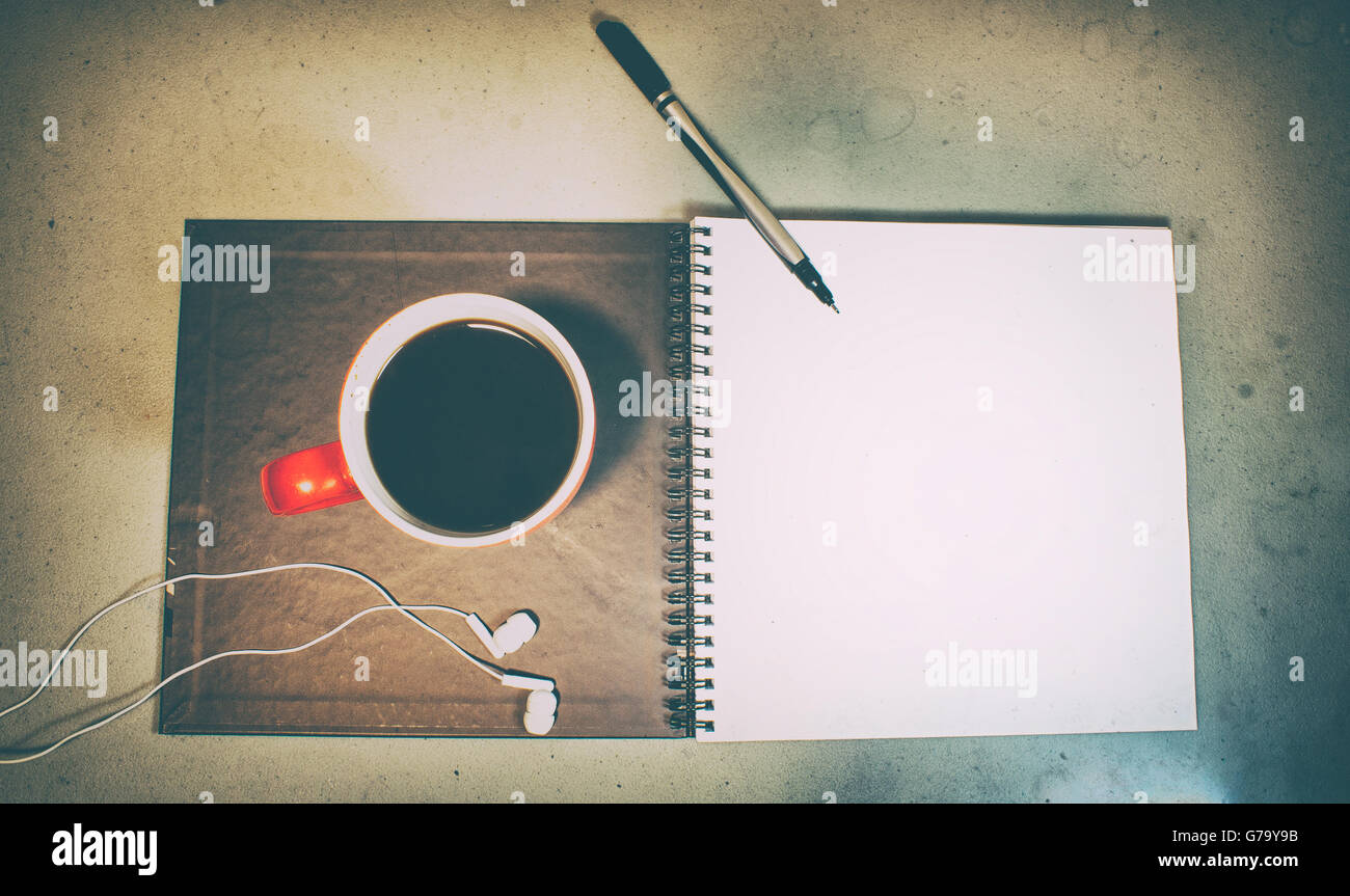 Fotografia di un quaderno, una tazza di soffee, una penna e un paio di auricolari, con un stile grunge Foto Stock
