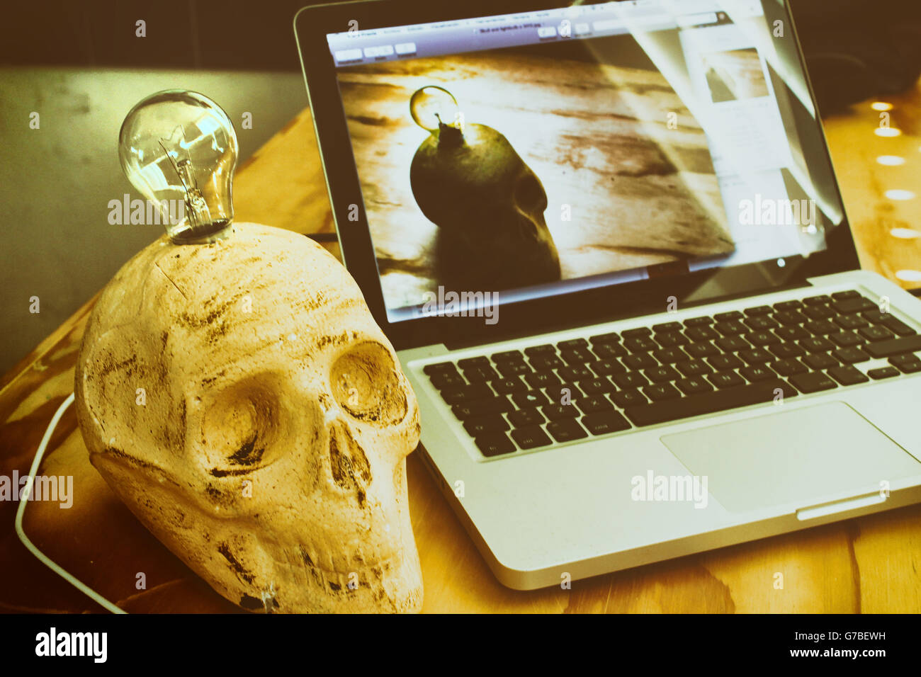Phoograph di un cranio con una lampadina elettrica e un computer portatile su una tavola di legno Foto Stock