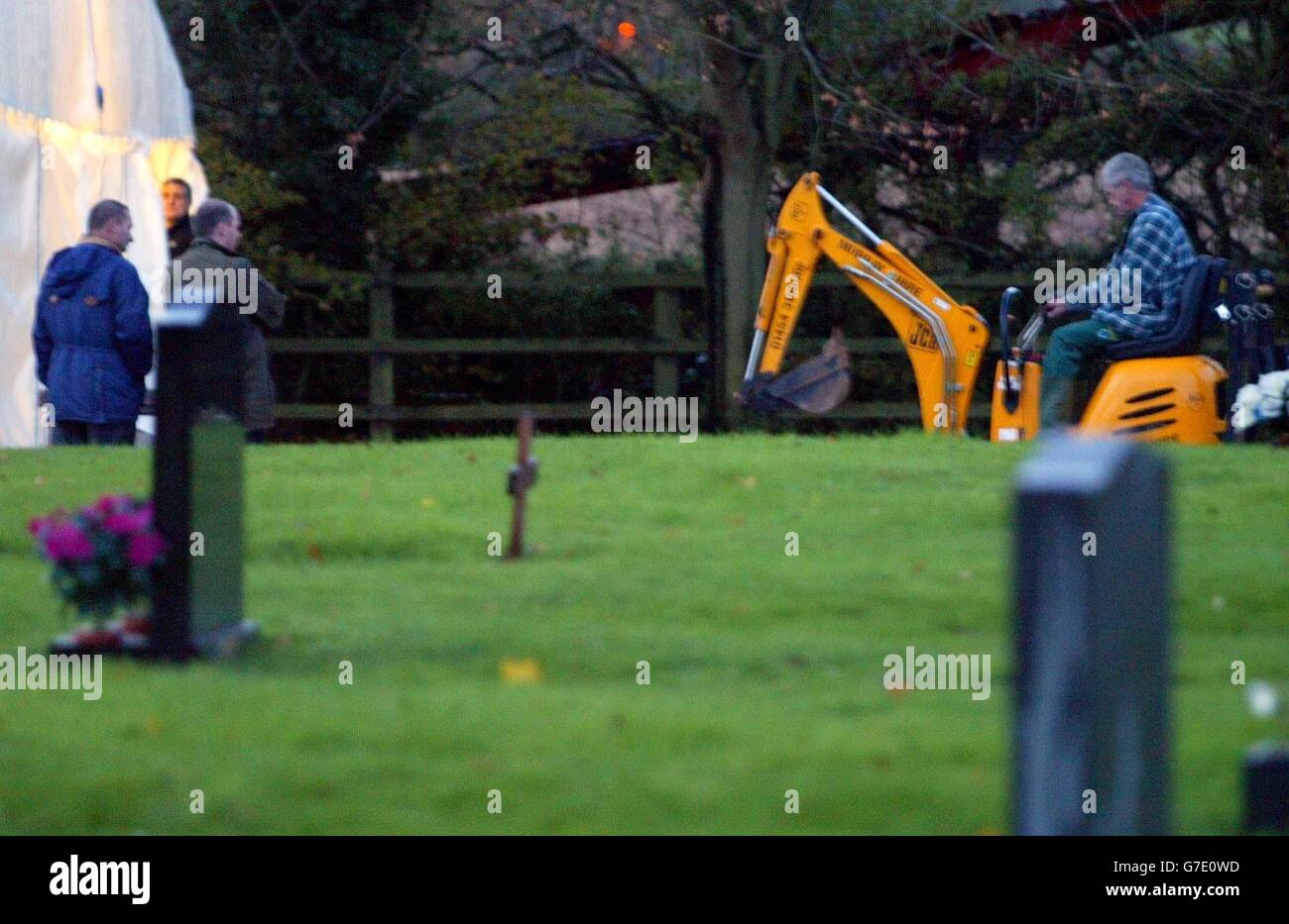 Gli ufficiali di polizia del Wiltshire portano in un digger al cimitero di Mayshill a Nibley, Nr Yate nel Gloucestershire del sud, mentre un marchese è messo sopra la tomba di Stephen Smith, il suo corpo deve essere scavato in su per l'esame di polizia. Foto Stock