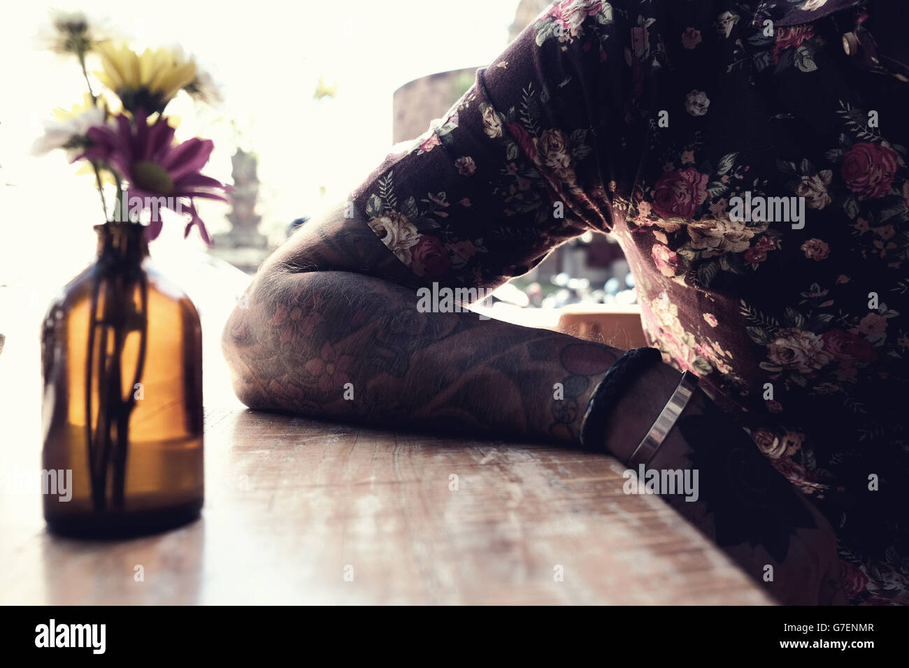 Tatuato uomo che poggia il braccio su un tavolo in un cafe in Ubud, Bali Foto Stock