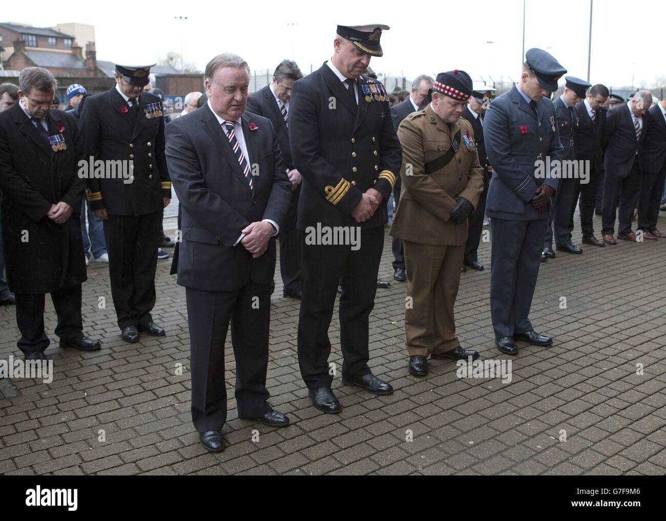 Il presidente dei Rangers David Somers (a sinistra) e i membri delle forze armate osservano un minuto di silenzio dopo aver posato una corona di papavero alla statua di John Greig per il Remembrance Day, Glasgow. Foto Stock