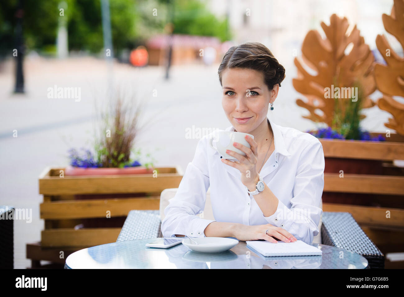 Pausa caffè. Attraente giovane imprenditrice nel convenzionale sorridere mentre in seduta cafè sul marciapiede e di bere il caffè. Foto Stock