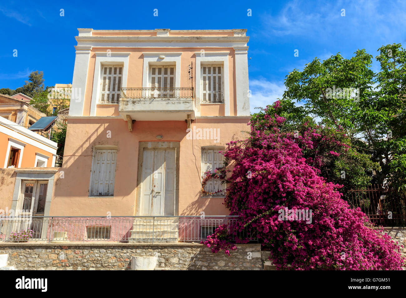 Vecchia casa a due piani con grandi rosa bougainvillea sull'isola greca di Symi. Foto Stock