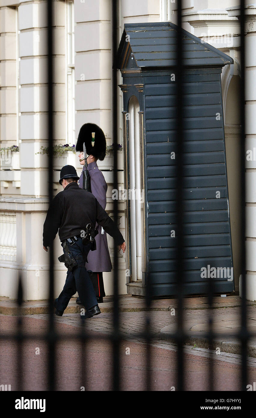Un ufficiale di polizia cammina passato una guardia in servizio all'interno delle porte che conducono al Mall, fuori Clarence House a Londra. Foto Stock