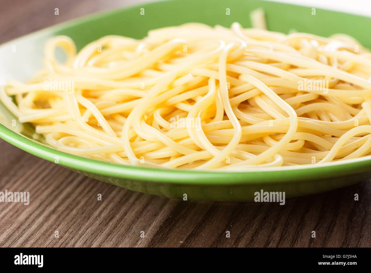 Cuocere gli spaghetti pianura servito in una piastra verde su un tavolo di legno Foto Stock