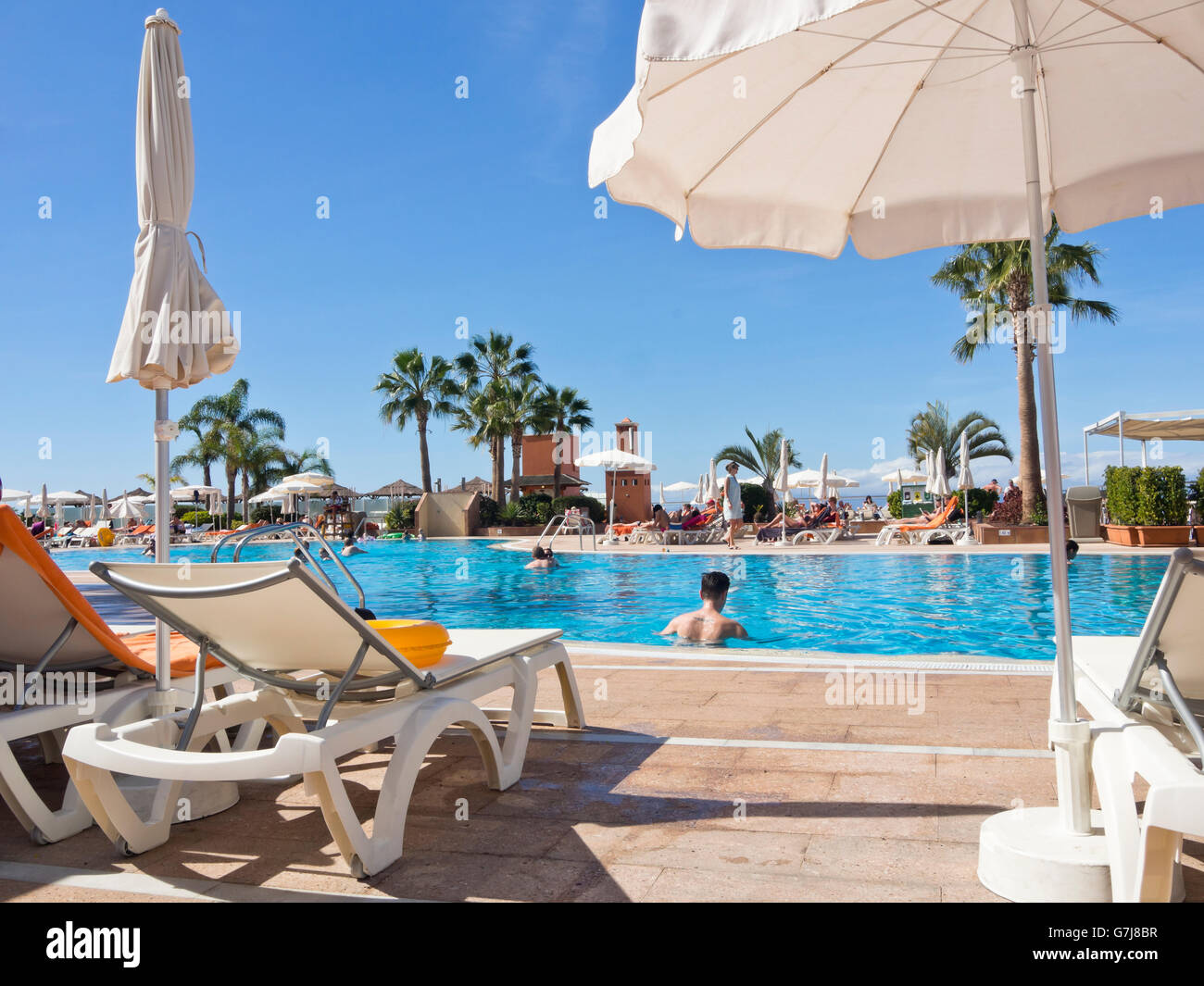 Vacanza da sogno per molti britannici pallido villeggianti un lettino a bordo piscina in Tenerife Canarie Spagna con cielo blu chiaro Foto Stock
