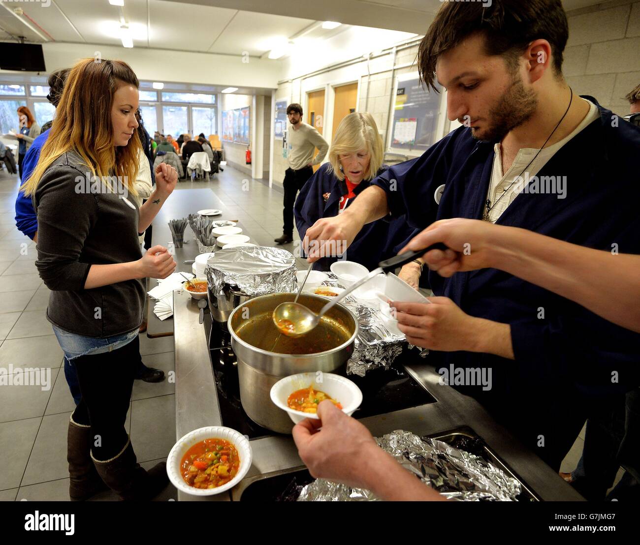 Un gruppo di volontari si allineano per servire ciotole di zuppa alla crisi al Shelter di Natale alla scuola di Haverstock a Camden, Londra del nord, dove le persone senza casa possono trovare cibo caldo, bevande calde e un posto per ottenere aiuto e consulenza. Foto Stock