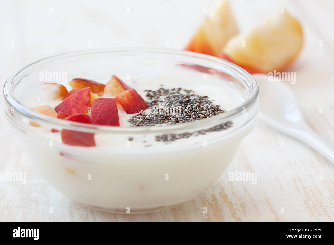 Yogurt con pesca in ciotola di legno bianco sullo sfondo. Dieta di luce prima colazione Foto Stock