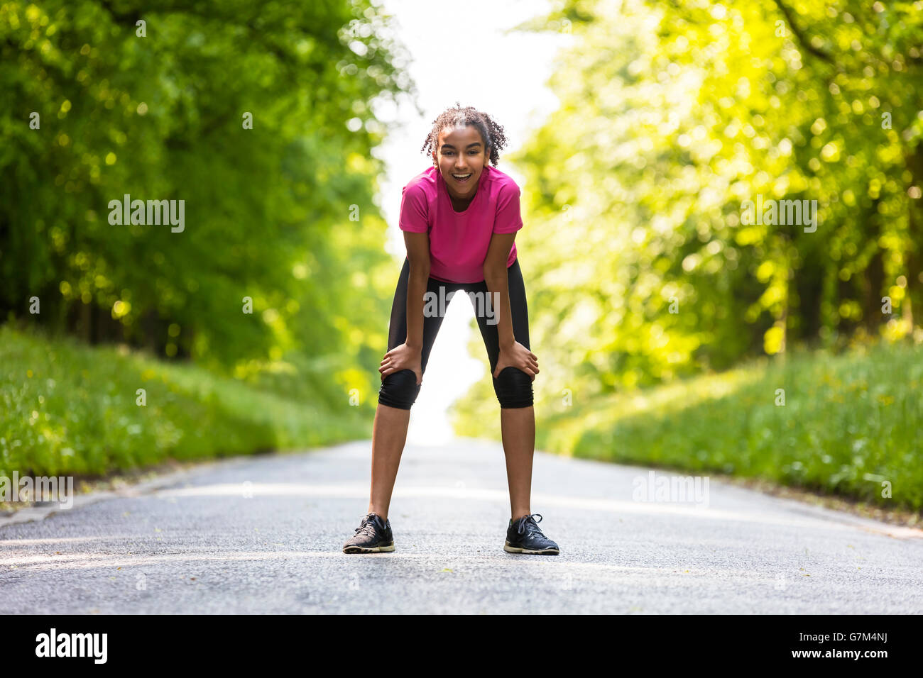 Bellissima gara di misto americano africano donna giovane ragazza adolescente fitness jogging in esecuzione su un rad rivestito di verde di alberi di estate Foto Stock
