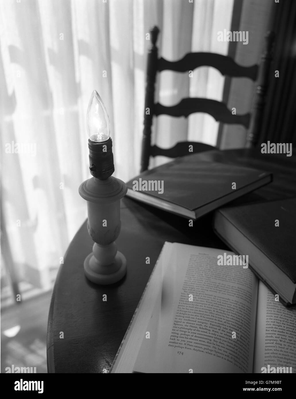 Lampada con nessuna ombra con un bulbo di fiamma su un tavolo. Un libro aperto e due libri chiusi sono anche sul tavolo. Foto Stock