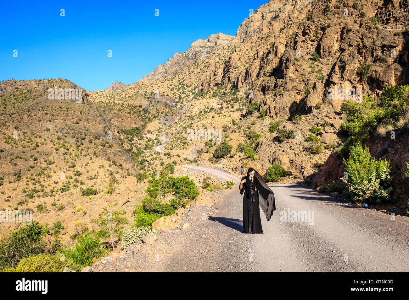 Una donna in nero abaya sta camminando su una strada in Al montagne Hajar in Oman Foto Stock