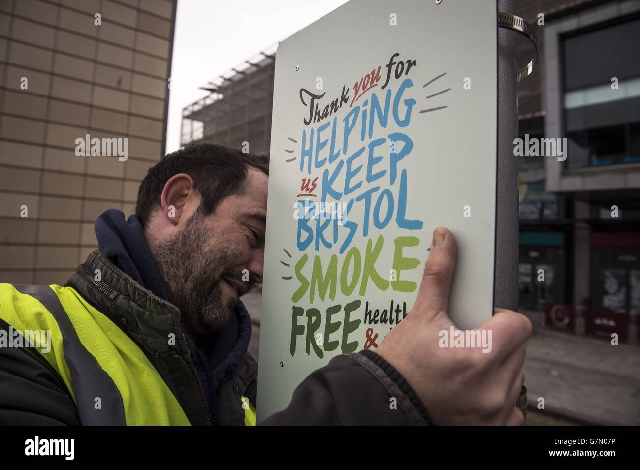 Un uomo fissa un segno ad un lampione in Millennium Square a Bristol, in quanto è uno dei due spazi pubblici per andare senza fumo come un pilota volontario è lanciato. Foto Stock