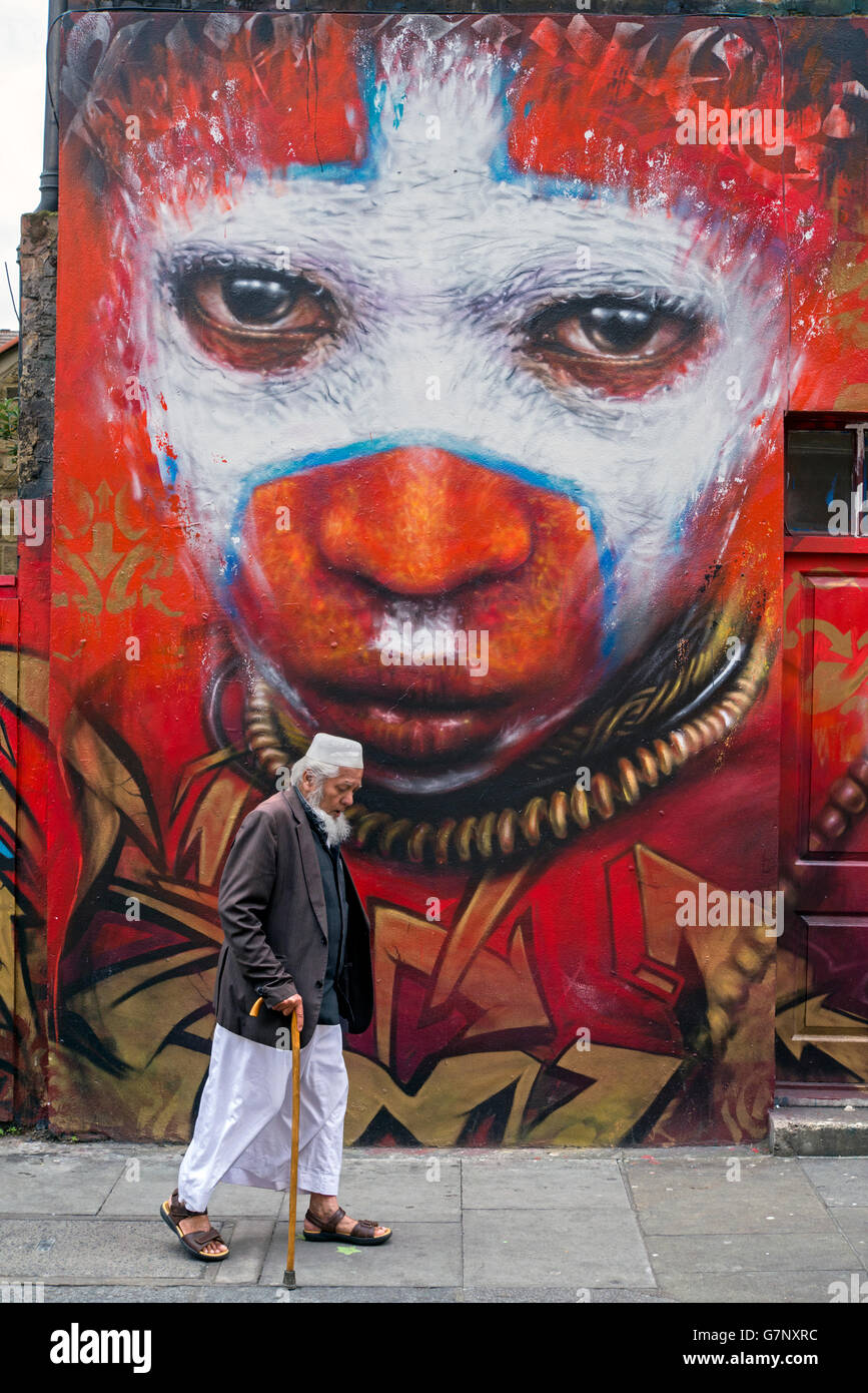 Un anziano uomo asiatico passeggiate da un pezzo di arte di strada da Dale Grimshaw in Hanbury Street, appena fuori la Brick Lane, Londra. Foto Stock