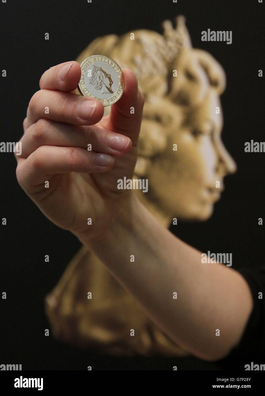 Un assistente dell'evento della zecca reale tiene una nuova moneta da due libbre davanti al ritratto di coniazione di Arnold Machin della regina Elisabetta II durante una cerimonia di inaugurazione dell'ultimo ritratto di coniazione della regina Elisabetta II alla National Portrait Gallery di Londra. Foto Stock