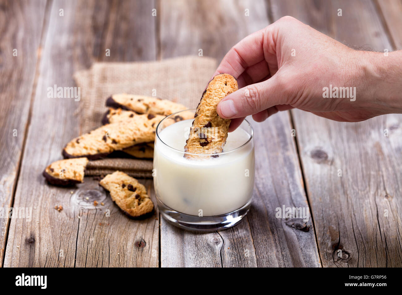 Stretta di mano immersione con pezzetti di cioccolato in un bicchiere di latte. Messa a fuoco selettiva sul pollice e cookie. Foto Stock Stretta di mano immersione con pezzetti di cioccolato in un bicchiere di latte. Messa a fuoco selettiva sul pollice e cookie. Foto Stock
