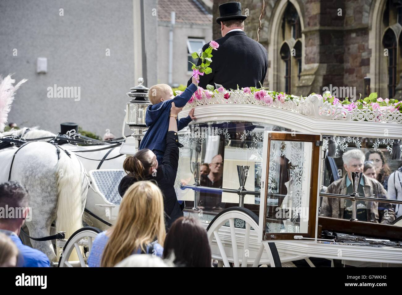 Un bambino piccolo è aiutato fino a mettere un fiori sulla cima del cuore bianco fuori della chiesa di Sant'Ambrogio a Whitehall, Bristol dopo il funerale del teenager Becky Watts. Foto Stock