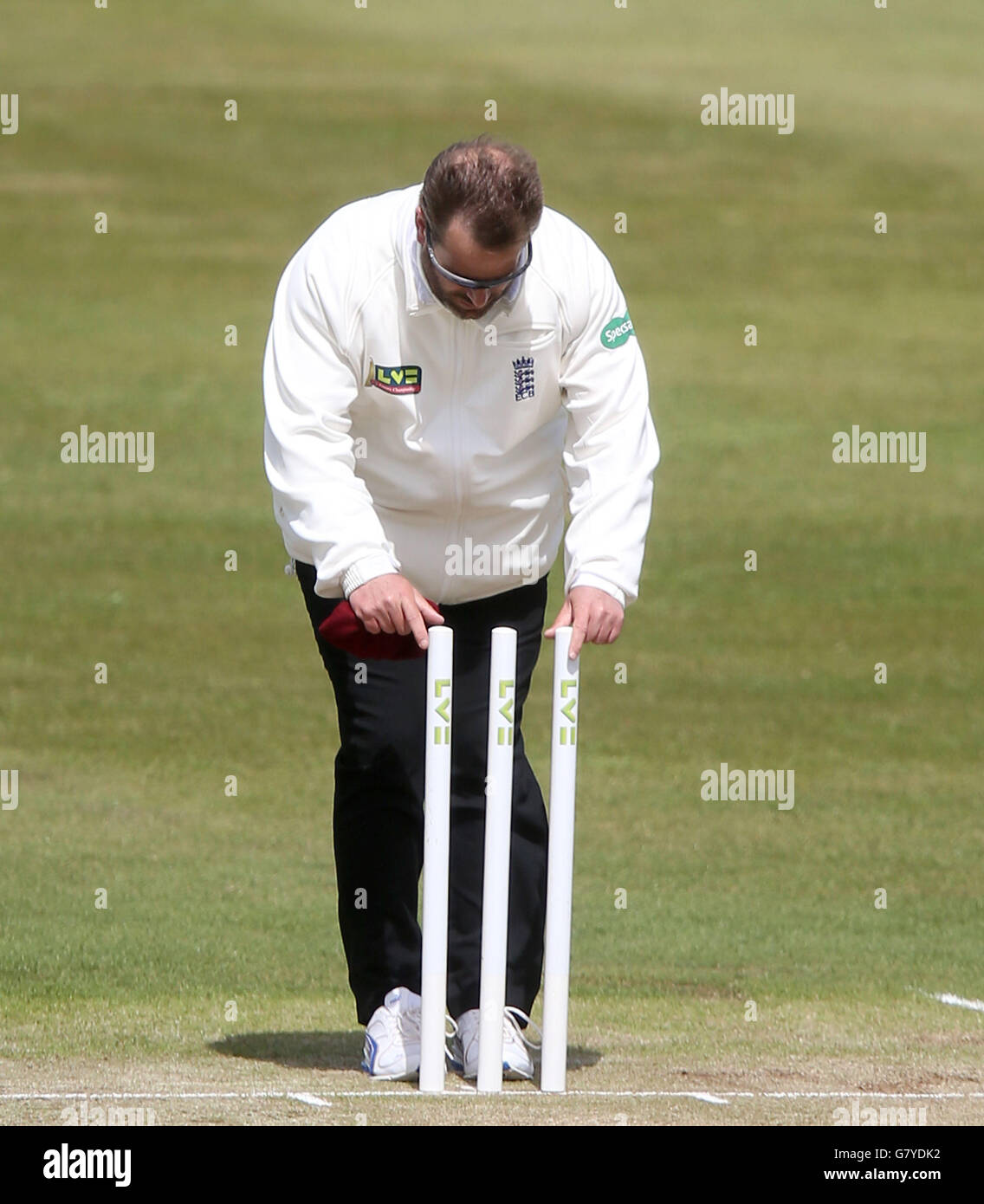 L'umpire Paul Baldwin riallinea i ceppi mentre il vento è a forte per usare le bails durante il campionato della contea di LV, la partita della seconda divisione al terreno della contea, Northamptonshire. Foto Stock