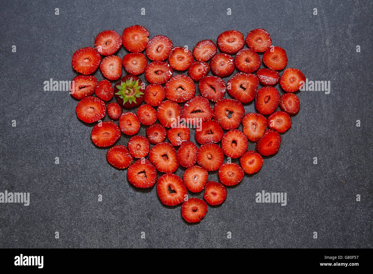 Fragole fresche fetta forma di cuore su sfondo nero Foto Stock