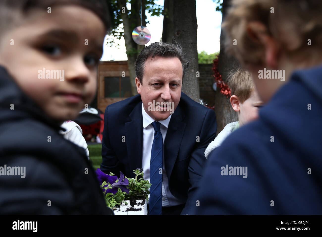 Il primo ministro David Cameron pianta fiori con bambini durante una visita in un vivaio per bambini a Londra, come ha ammesso Cameron 'ci vorrà tempo? Per ottenere piani di raddoppiare la fornitura gratuita di assistenza all'infanzia tra avvertimenti il sistema deve affrontare 'deltdown? A meno che i cambiamenti non siano pienamente finanziati. Foto Stock