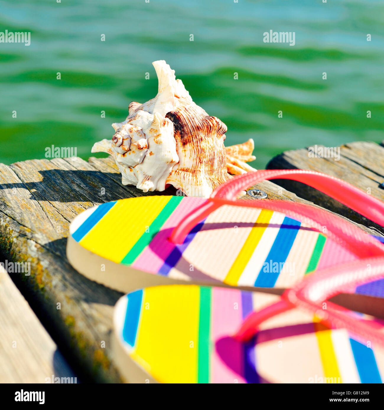 Primo piano di una coppia di colorati flip-flop e un conch su un weathered molo in legno sul mare Foto Stock