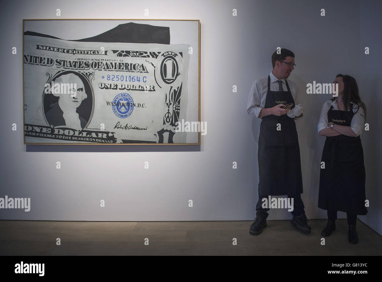 Gli assistenti della galleria si affiancano al 'Silver Certificate, 1962' di Andy Warhol, stimato a 13-18 milioni di sterline, durante l'anteprima di stampa di 'al portatore su richiesta', una collezione privata di 21 opere ispirate dal dollaro statunitense da artisti tra cui Andy Warhol a Sotheby's, Londra. Foto Stock