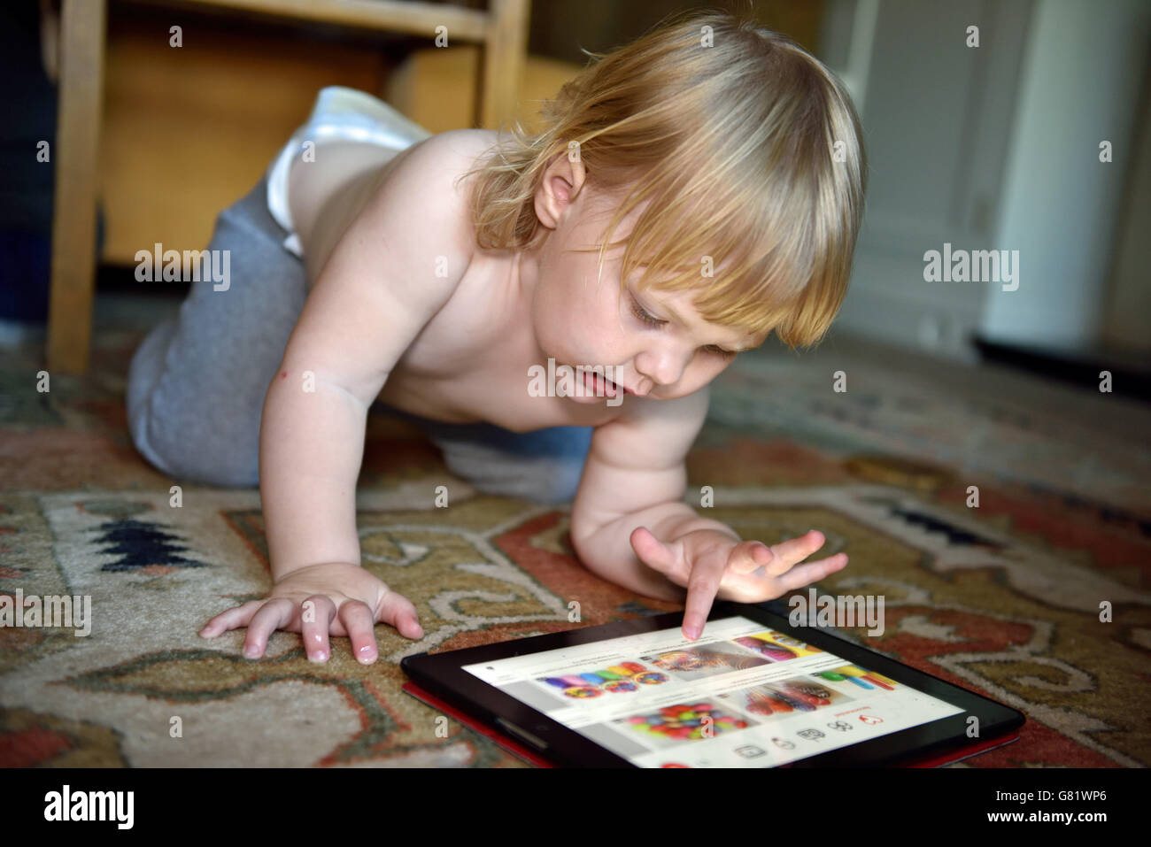 Un bambino a casa accovacciato sul pavimento, concentrandosi sulla scelta di un gioco sul suo ipad. Foto Stock