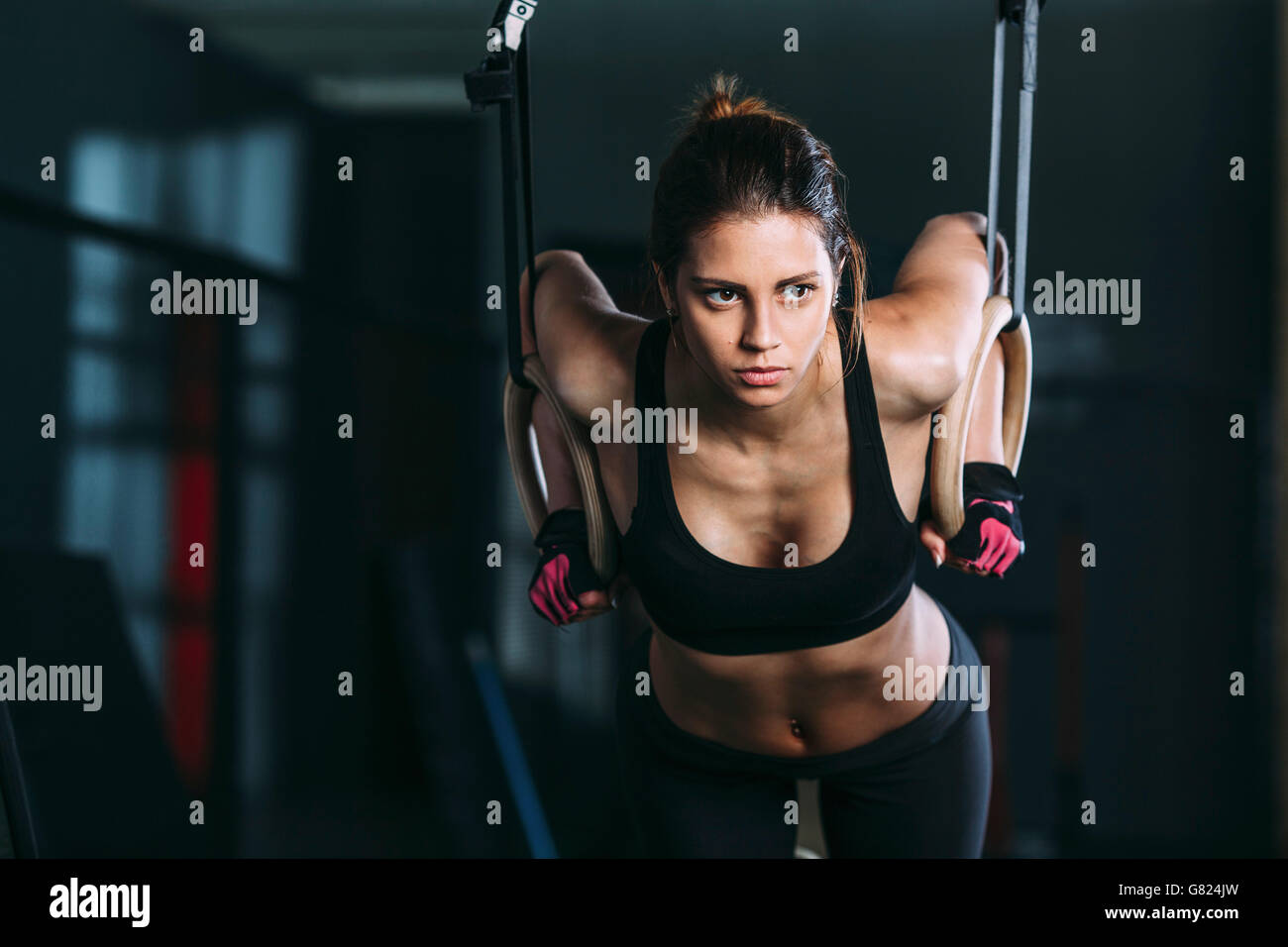 Vista frontale della donna appesa su anelli di ginnastica in palestra Foto Stock