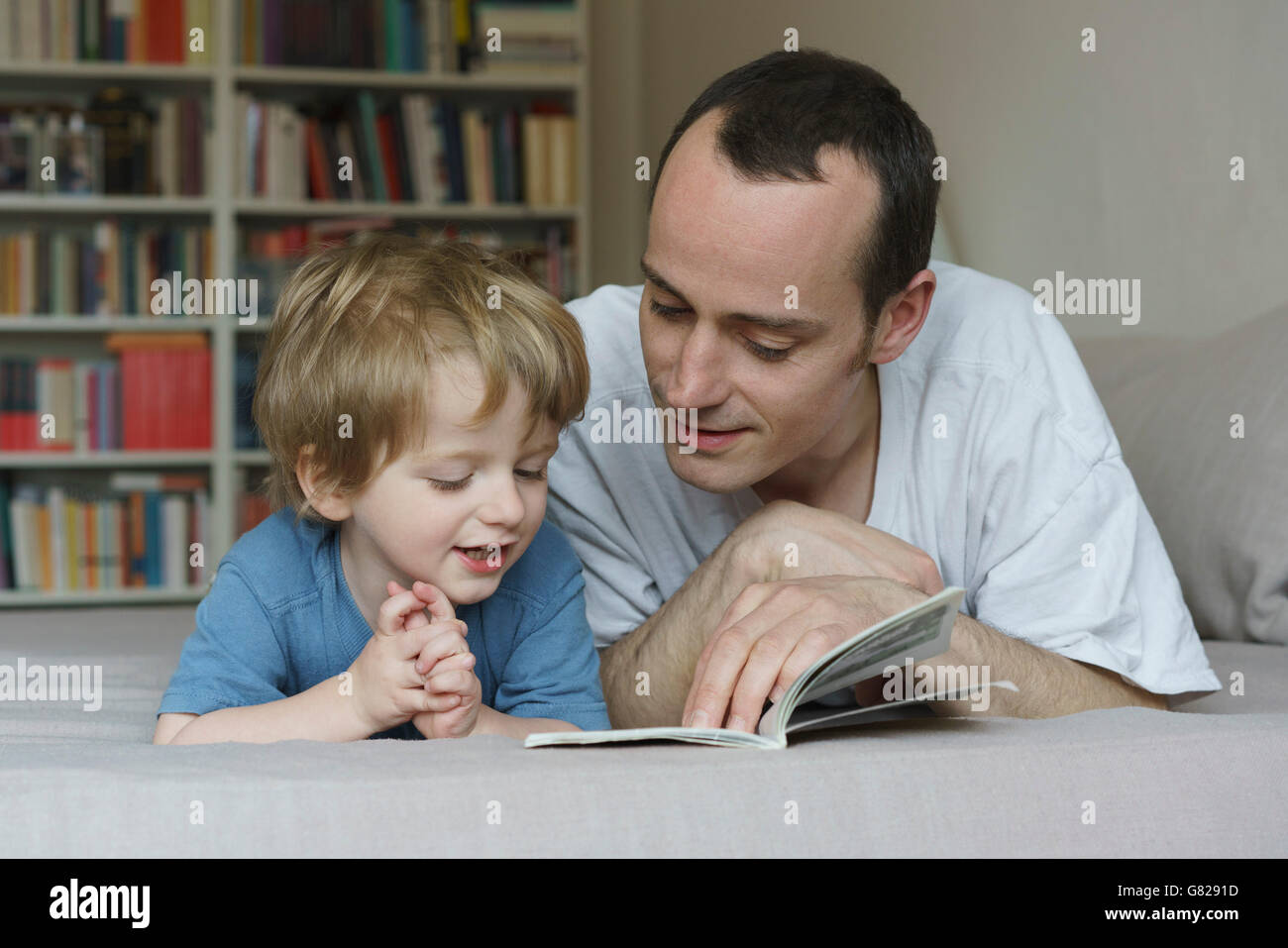 Padre e figlio libro lettura mentre giaceva sul letto di casa Foto Stock