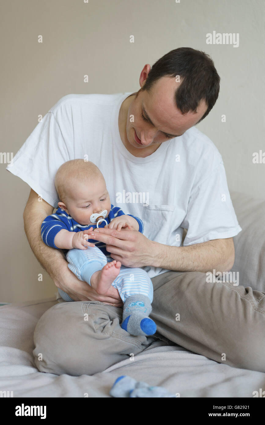 Vista frontale del padre che porta il figlio mentre è appoggiato sul letto di casa Foto Stock