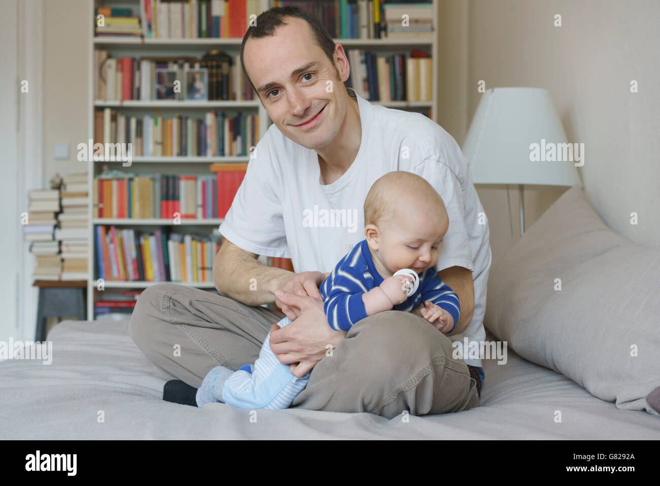 Padre e figlio seduti sul letto contro scaffale a casa Foto Stock