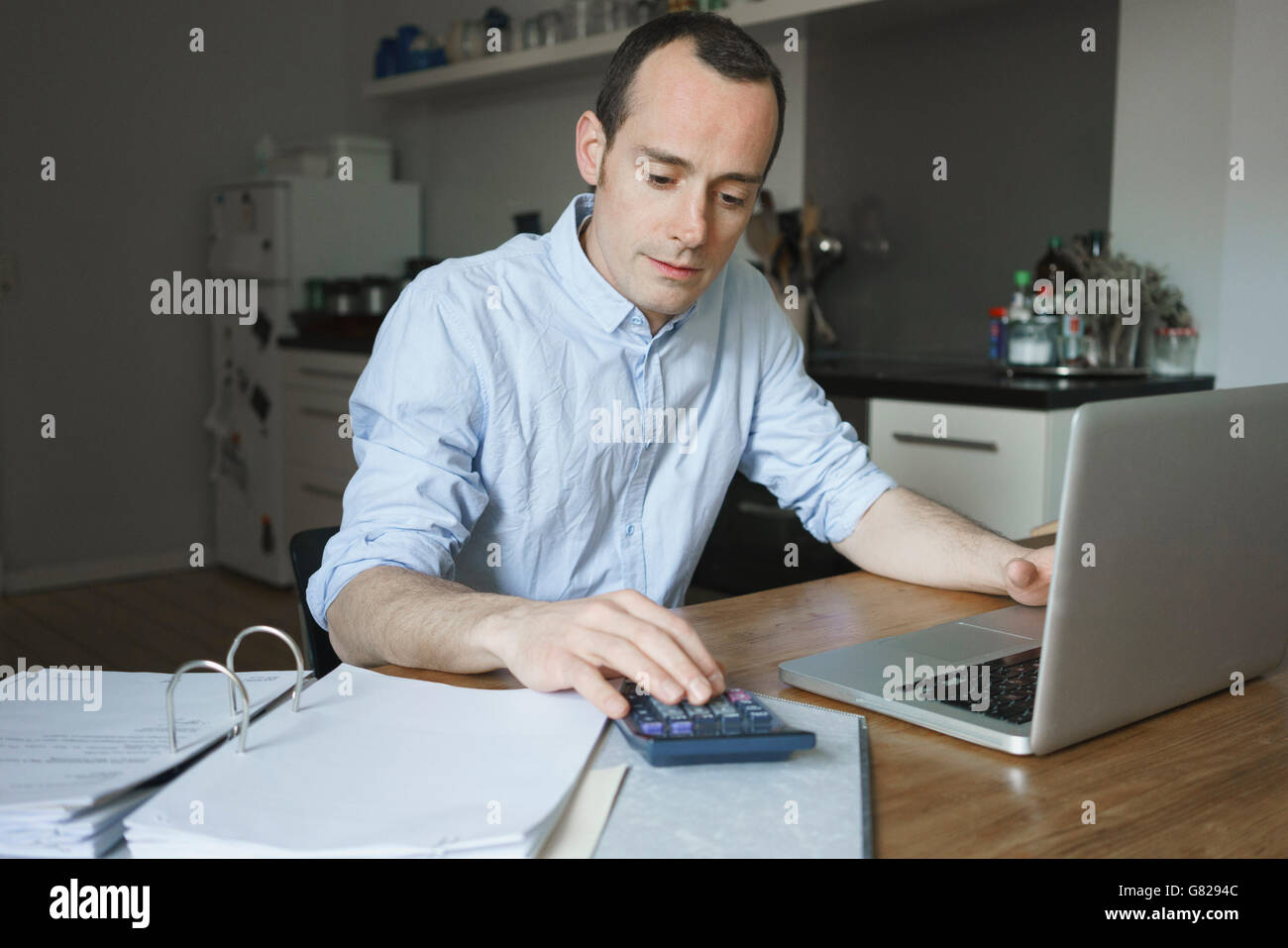 Grave uomo che lavora su documenti con computer portatile e calcolatrice a casa Foto Stock