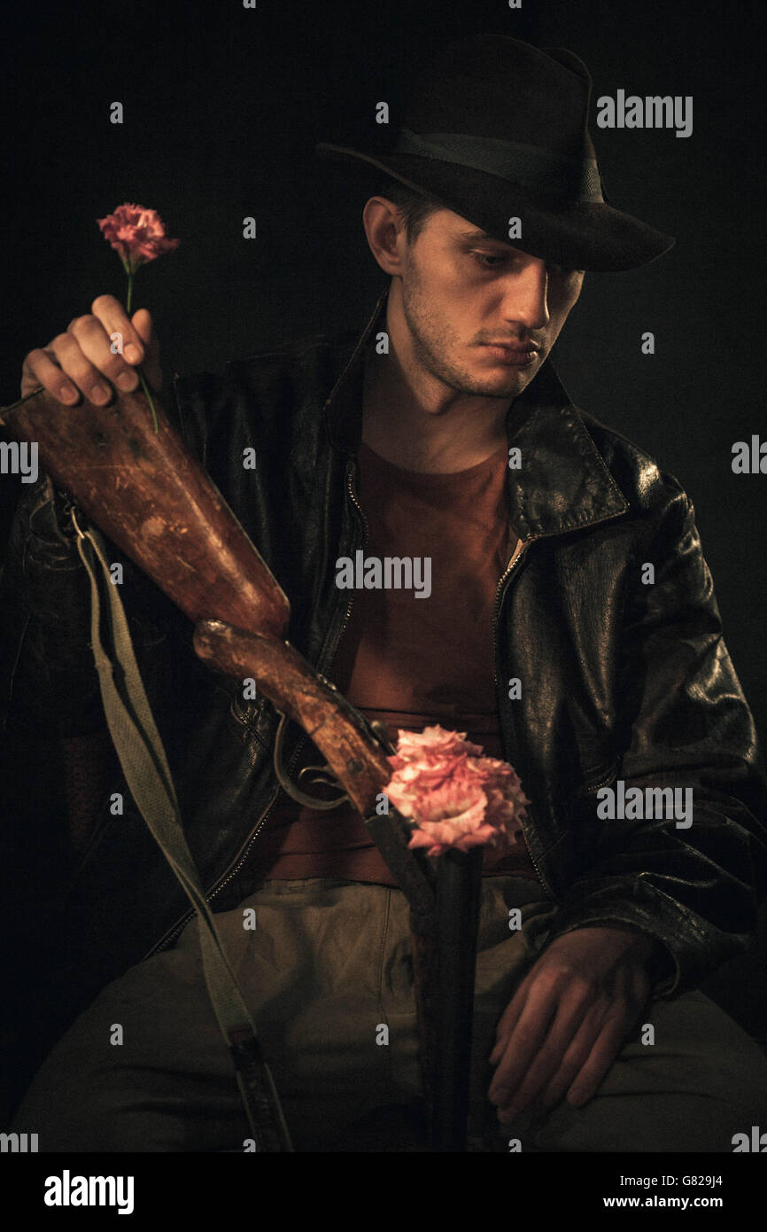 Riflessivo cowboy holding rose e il fucile su sfondo grigio Foto Stock
