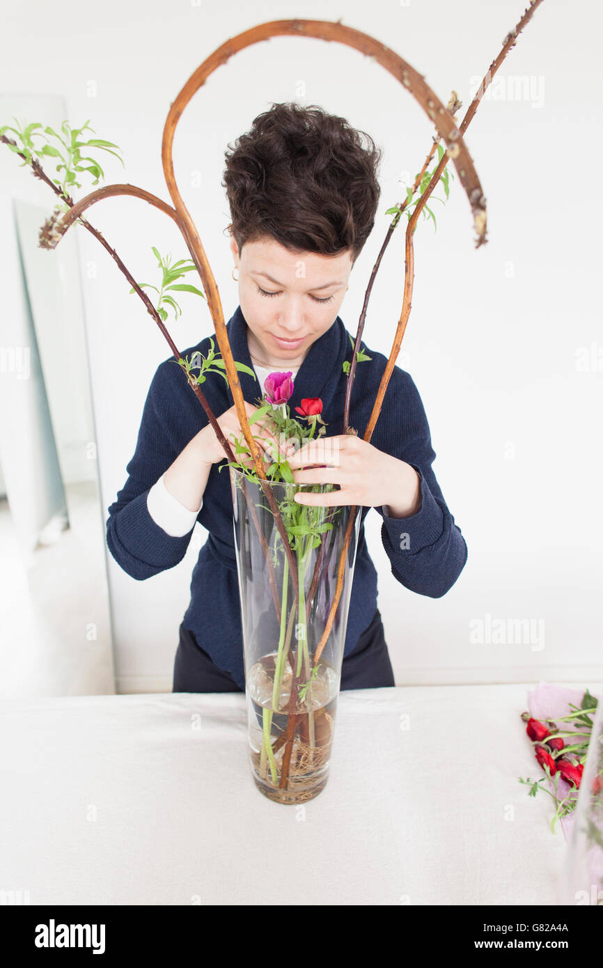 Metà donna adulta disponendo dei fiori in vaso sul tavolo a casa Foto Stock