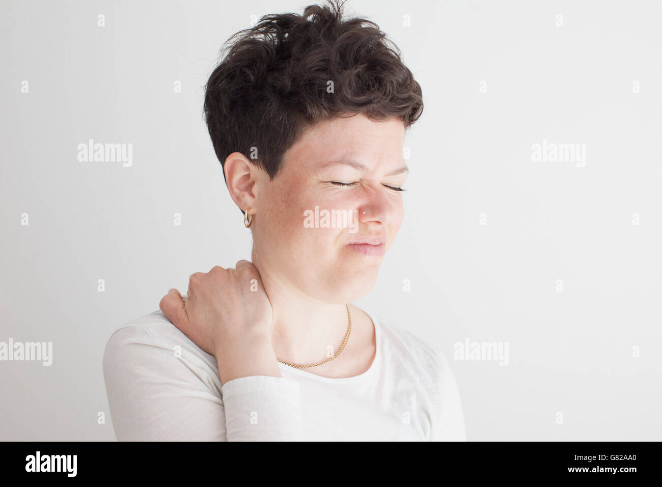 Close-up di metà donna adulta che soffrono di dolore alla spalla contro uno sfondo bianco Foto Stock