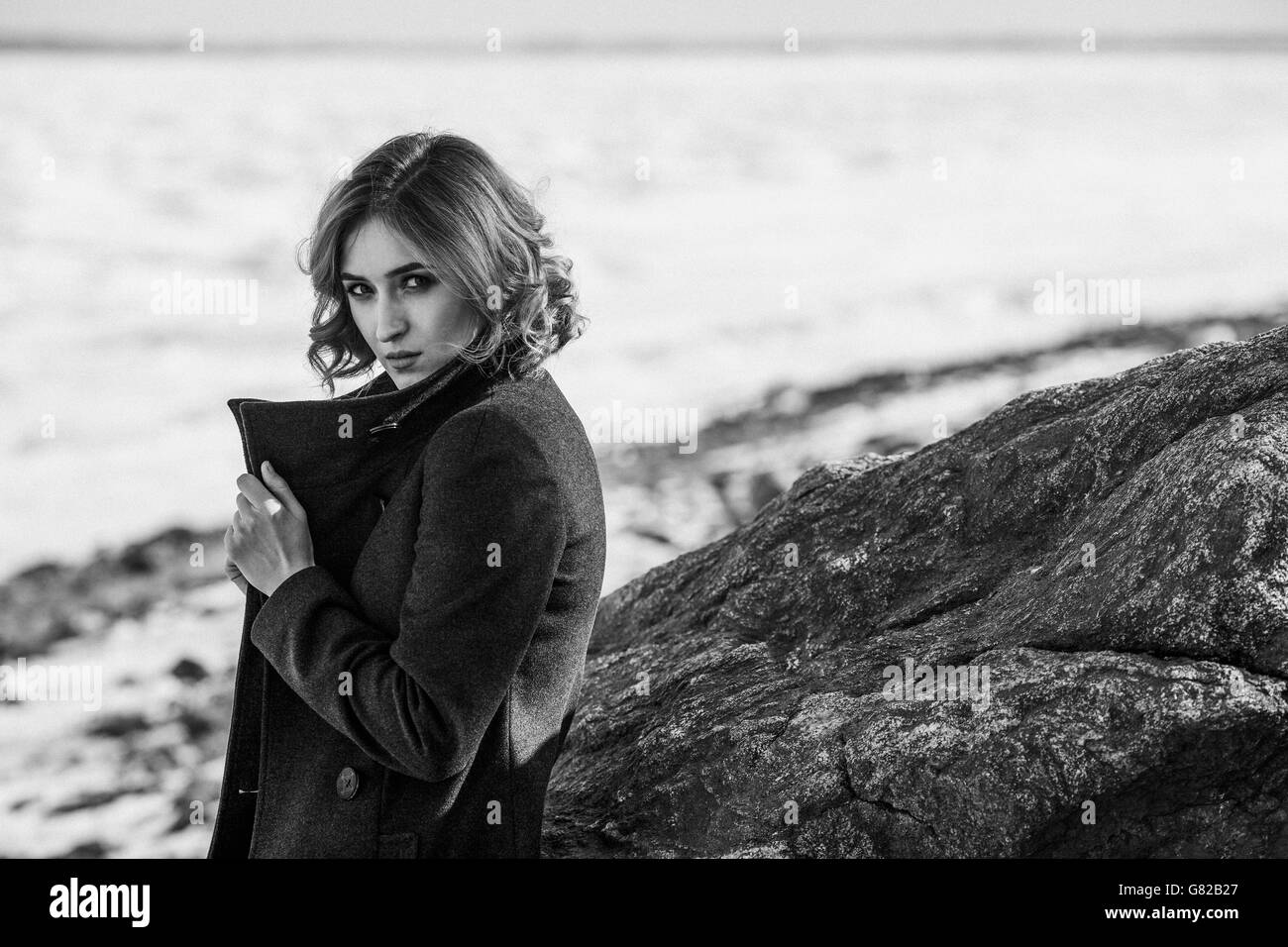 Ritratto di giovane e bella donna che indossa cappotto invernale mentre in piedi da rock Foto Stock