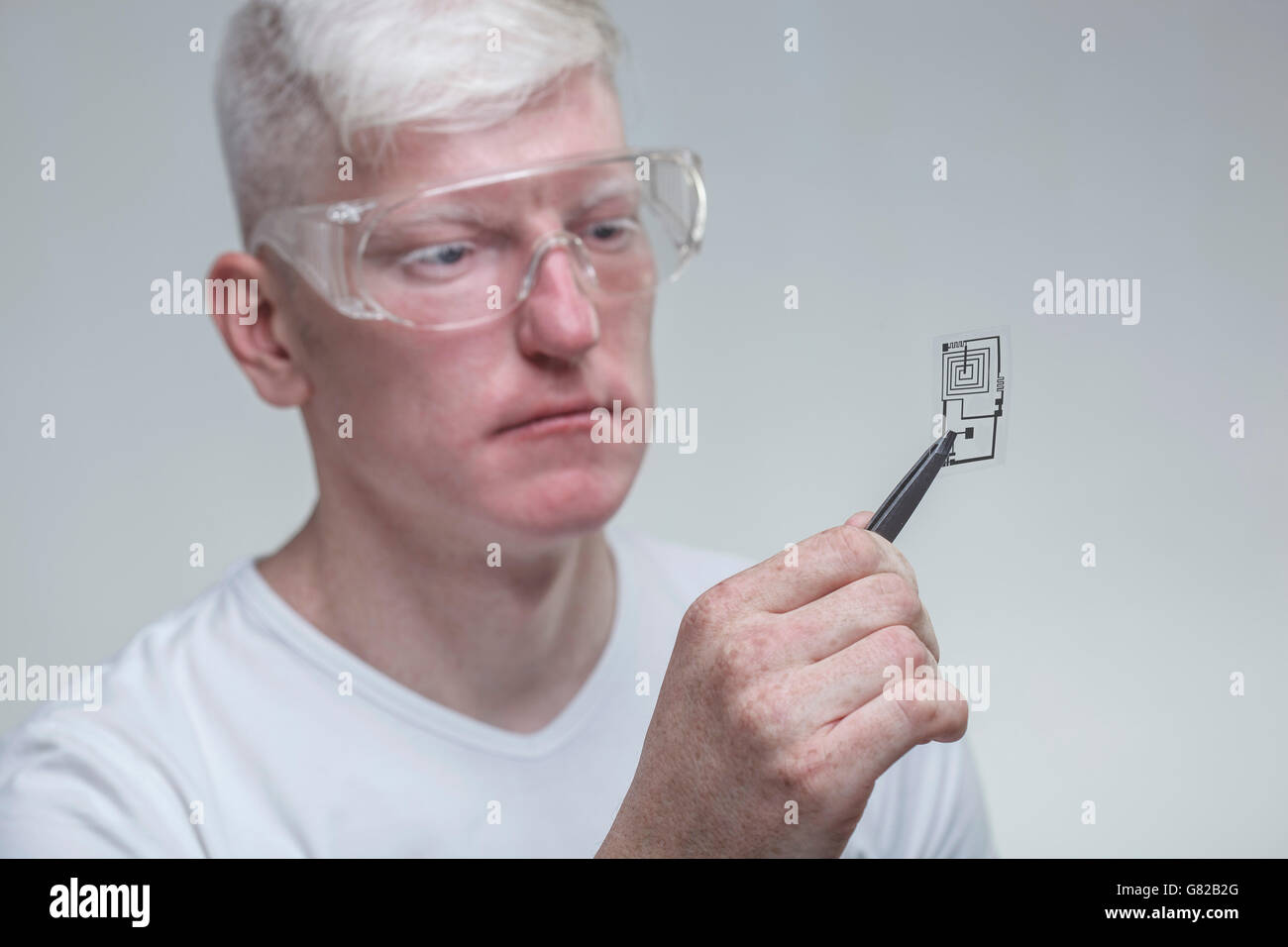 Albino uomo indossare occhiali protettivi durante l'esame chip contro uno sfondo grigio Foto Stock