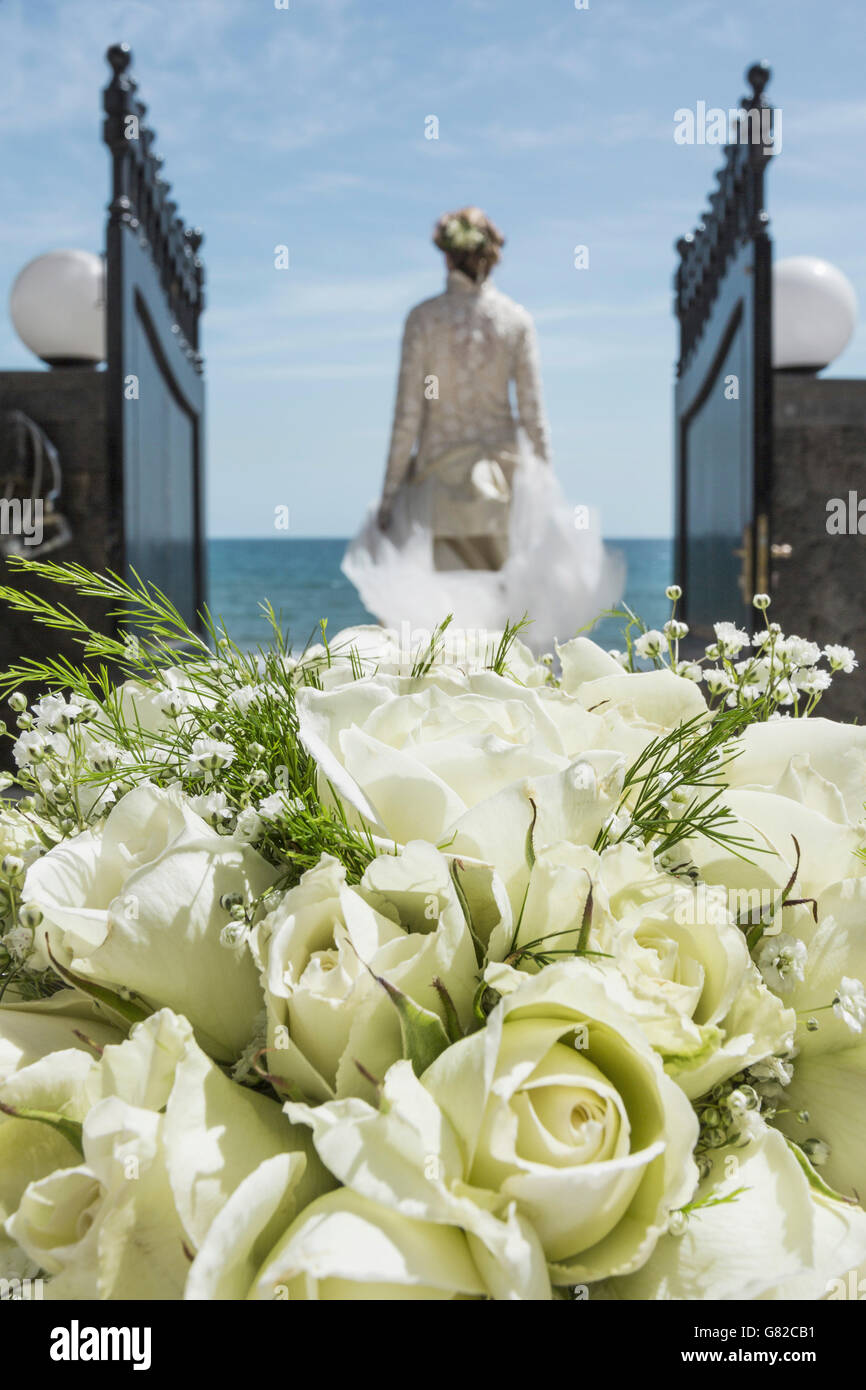 Vista posteriore della sposa passeggiate verso la spiaggia con focus su bouquet di rose in primo piano Foto Stock