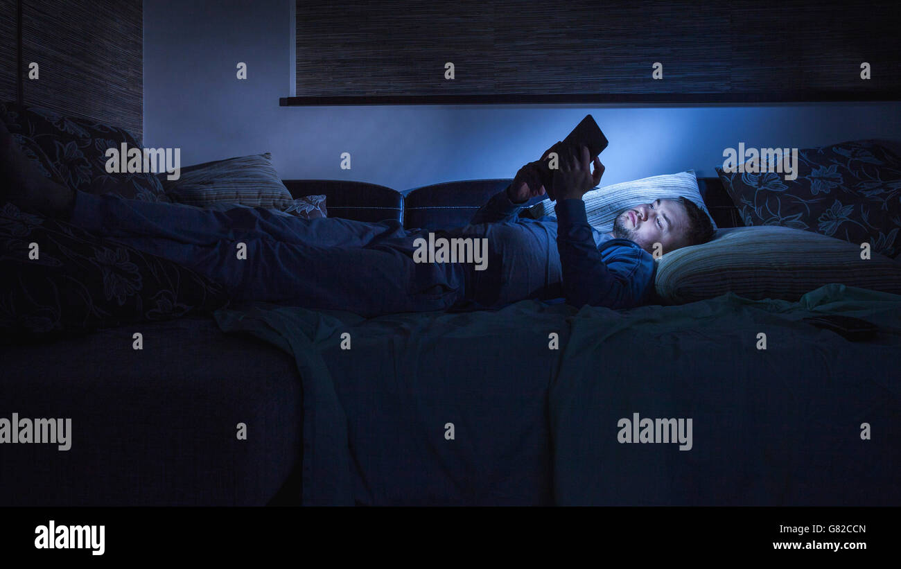 Uomo con tavoletta digitale mentre si riposa sul divano nel buio a home Foto Stock