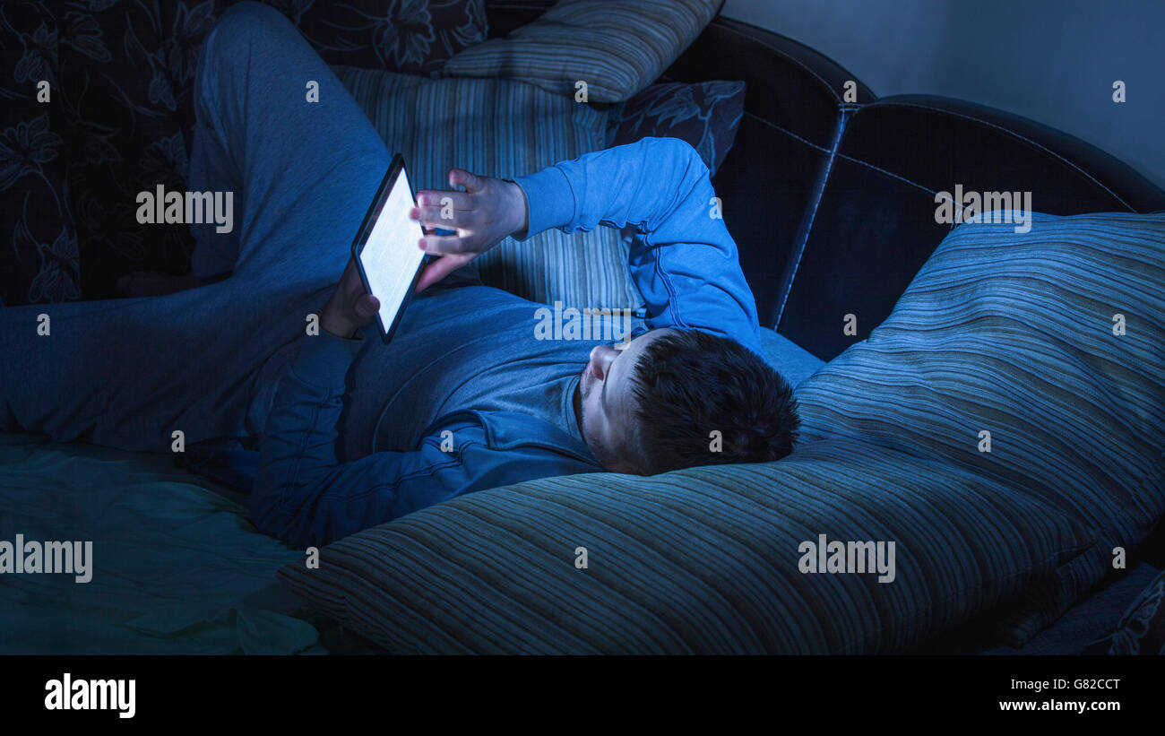 Uomo navigare in internet sulla tavoletta digitale mentre si riposa sul divano di casa Foto Stock