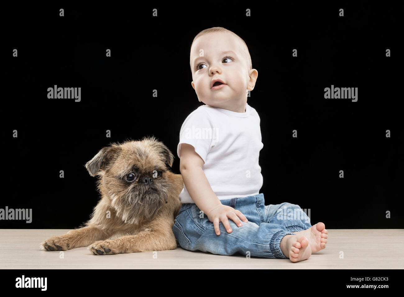 Carino ragazzo seduto con il cane sul tavolo su sfondo nero Foto Stock