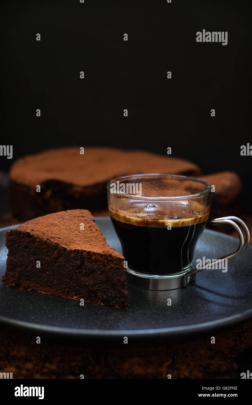 Una fetta di flourless olio d'oliva torta al cioccolato con una tazza di caffè caldo su una piastra nera. Cibo scure della fotografia. Foto Stock