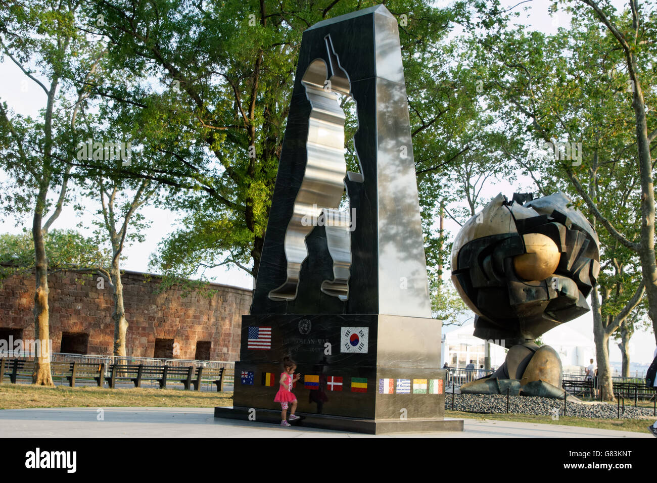Una ragazza ha giocato nella batteria accanto al monumento ai caduti della guerra di Corea e la sfera dal sito del World Trade Center. Foto Stock
