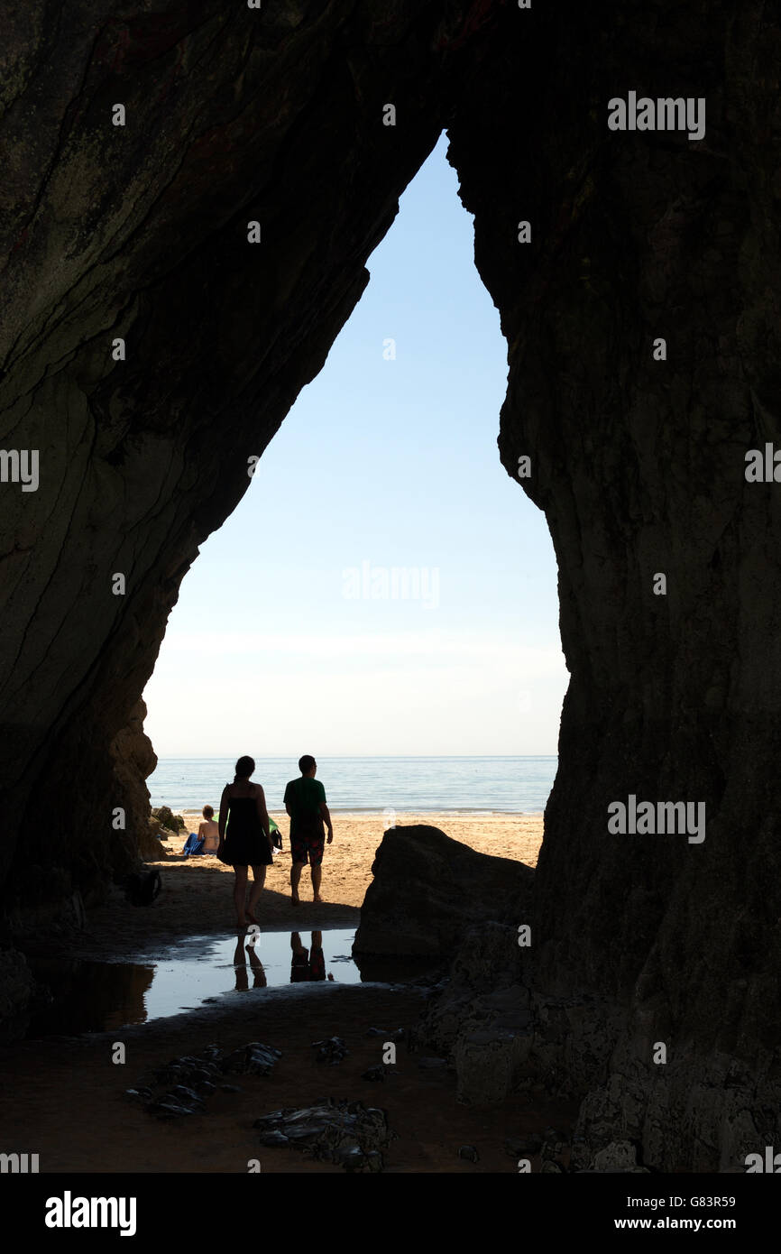 Uscendo da una grotta sulla spiaggia e due persone scoprono la meraviglia di Gower attraverso questo gateway naturale Foto Stock