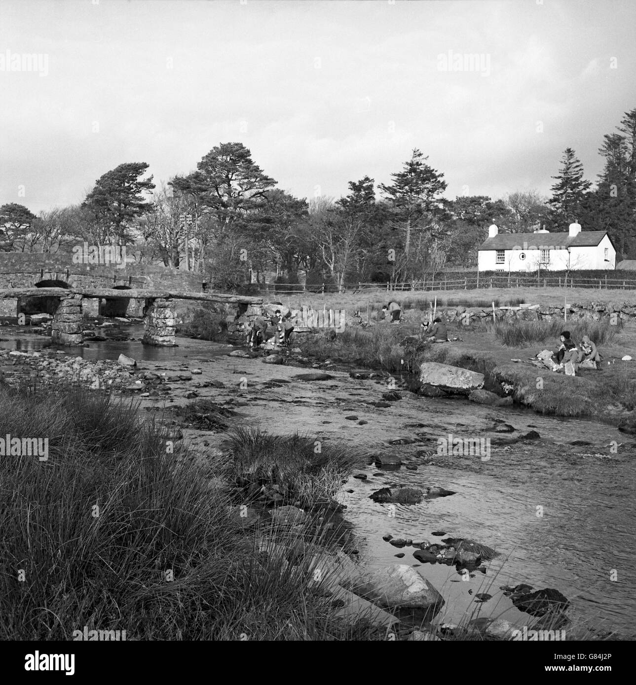 Gruppi di escursionisti pranzano presso il fiume East Dart vicino al vecchio ponte di clapper a Postbridge, Dartmoor. Foto Stock