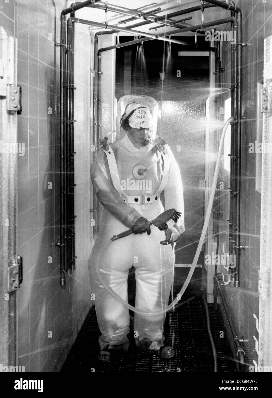 Dopo aver lavorato come operatore in un'area attiva dell'Active Handling Building presso lo stabilimento di ricerca sull'energia atomica di Winfrith, Dorset, una donna si strofina con i suoi indumenti protettivi sotto getti d'acqua. Foto Stock