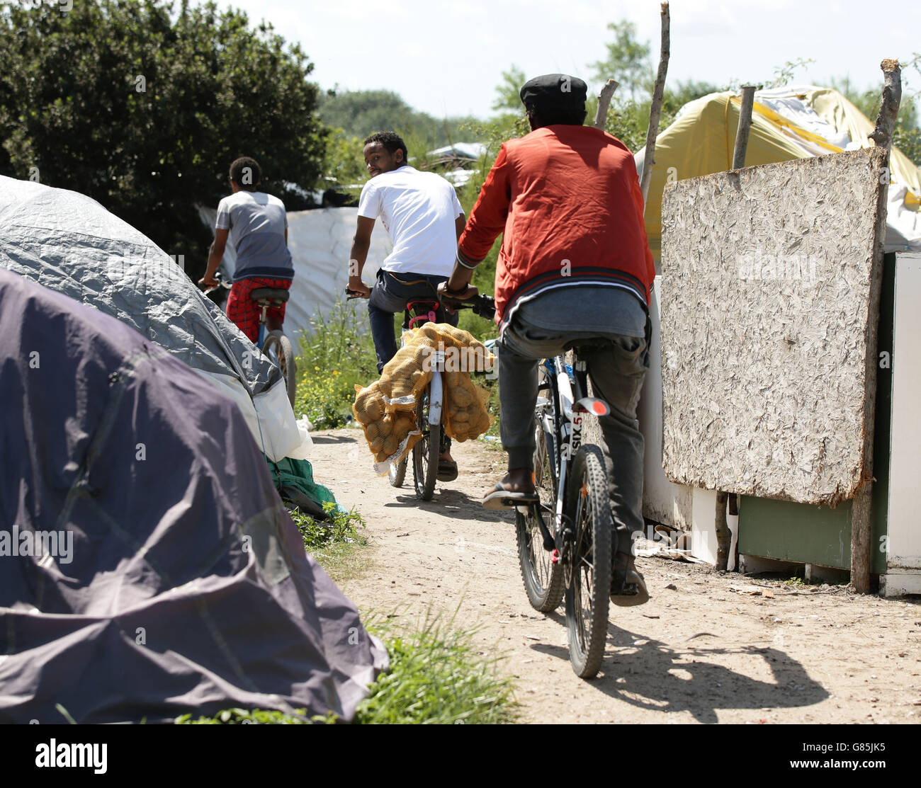 Un uomo usa una bicicletta per trasportare sacchi di patate nel campo migrante conosciuto come la nuova giungla a Calais, Francia. Foto Stock