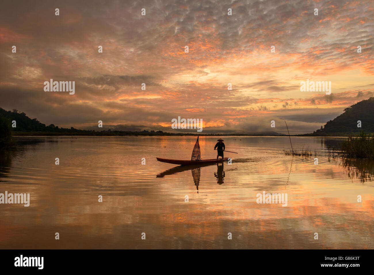 Uomo in piedi in barca da pesca al tramonto, il fiume Mekong, Thailandia Foto Stock