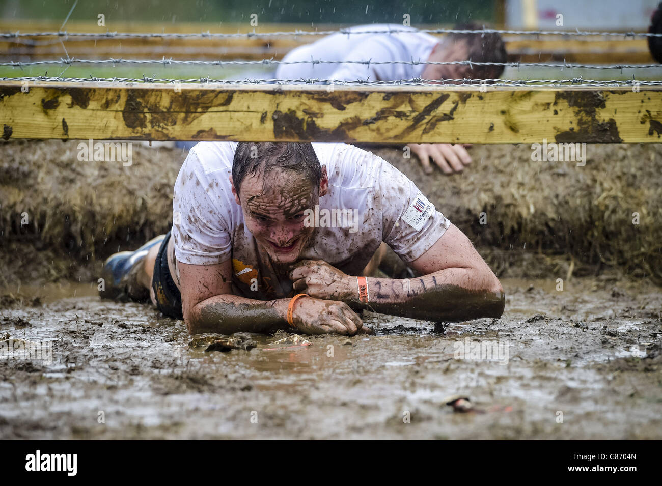 I partecipanti potranno sguazzare sotto una trincea coperta di filo spinato durante un evento di 12 km di percorso a ostacoli Mudder a Cirencester, Wiltshire. Foto Stock